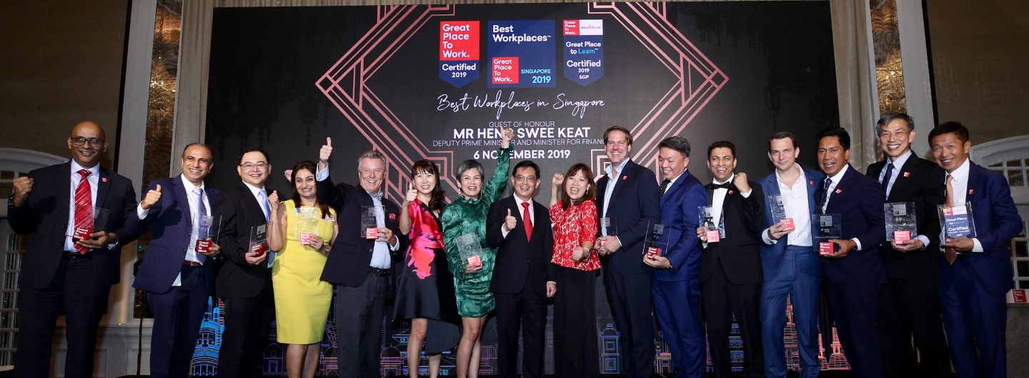People holding Great Place to Work awards stand before a "Best Workplaces in Singapore" backdrop.